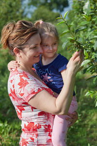 Smiling mother with daughter touching plants at agricultural field