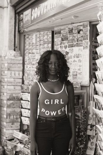 PORTRAIT OF YOUNG WOMAN STANDING AGAINST BUILDING