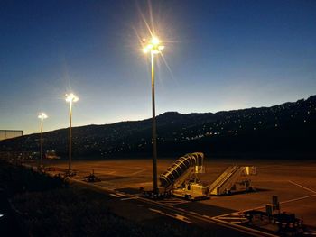 Illuminated road by mountains against clear sky