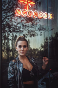 Portrait of woman standing against illuminated sign at night