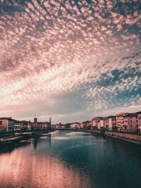 Bridge over river by buildings in town at sunset