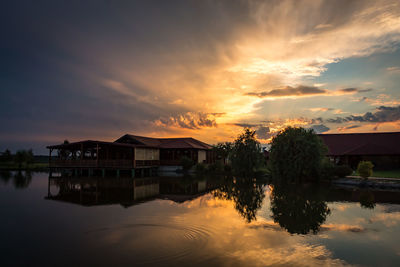 Houses by lake and buildings against sky during sunset