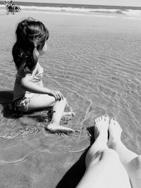 Low section of mother with daughter sitting at beach during sunny day