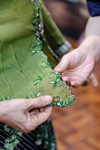 Midsection of women analyzing embroidery on green fabric