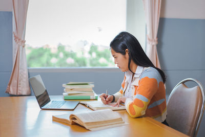 Woman reading book while sitting on table