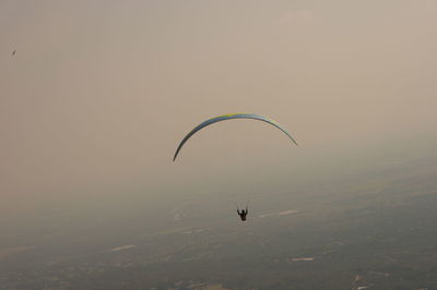 Person paragliding over sea against sky during sunset