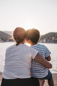 Rear view of son kissing mother at beach against sky