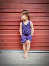 Full length of cute girl looking away while leaning against wall