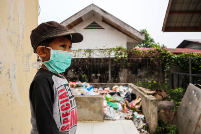 Side view of boy wearing pollution mask while standing on sidewalk