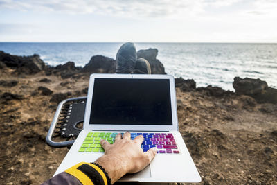 Cropped hand of man touching laptop at beach