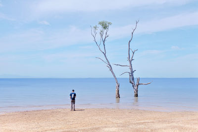 Rear view of man standing at beach against sky