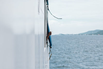 Man smoking by window of nautical vessel on sea against sky