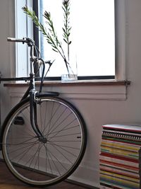 Bicycle parked safely inside house next to stack of book against window wall