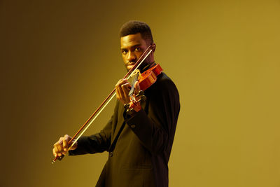 Midsection of man playing violin against yellow background