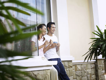 Smiling couple talking while having coffee against wall