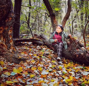 Woman sitting on tree in forest during autumn