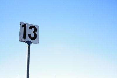 Low angle view of road sign against clear blue sky