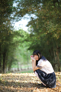 Portrait of woman crouching on land against trees