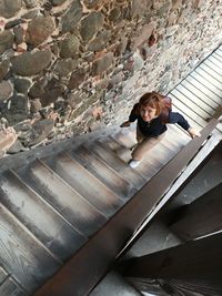 Portrait of smiling young woman moving up on steps by stone wall