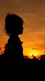 Portrait of silhouette little girl against orange sky