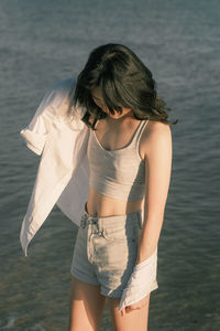 Young woman standing at beach. short jeans, white blouse and black hair