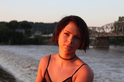 Portrait of teenage girl sitting against river during sunset
