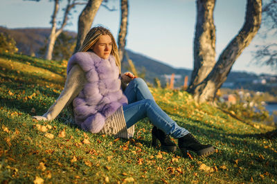 Thoughtful young woman sitting on field at public park