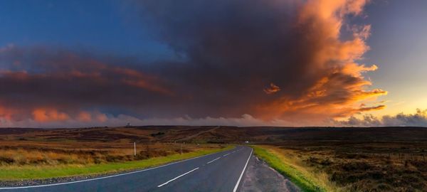 Empty road amidst moors against sky during sunset