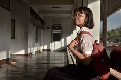 Side view portrait of young woman standing in corridor at school