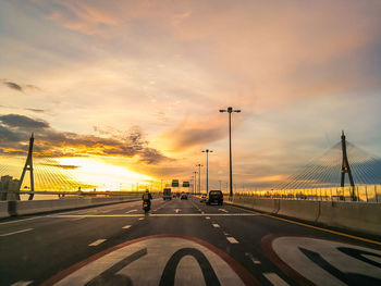 Cars on road in city against sky during sunset