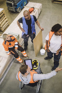 Blue-collar worker sitting on wheelchair instructing colleagues in warehouse