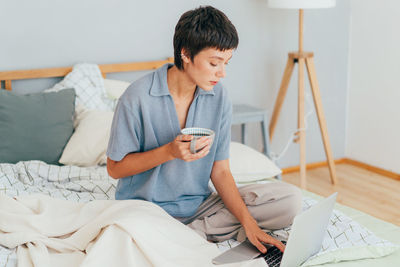 Young woman using mobile phone while lying on bed at home