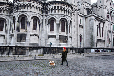 A blonde parisian girl in a red beret walking her pet corgi dog in montmartre on a winter afternoon.