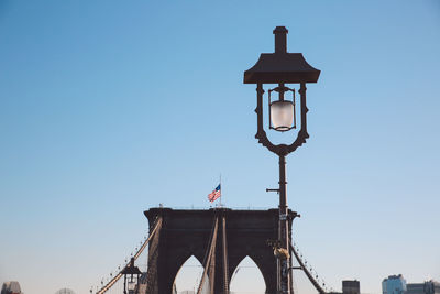Lamp post by brooklyn bridge against clear blue sky in city