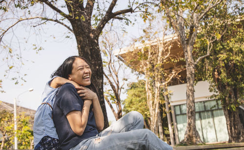 Low angle view of women sitting on plant against trees