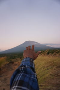 Midsection of person on landscape against sky during sunset