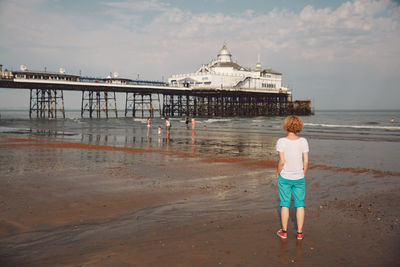 Rear view of woman standing by eastbourne pier at beach against sky