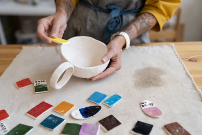 Ceramist workplace female potter choosing color for cup painting from palette in studio, close up