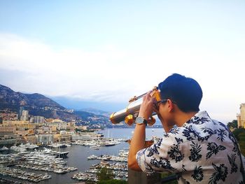 Man using coin-operated binoculars while standing against harbor