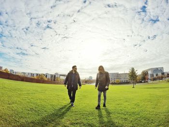 Men walking on grassy field against cloudy sky