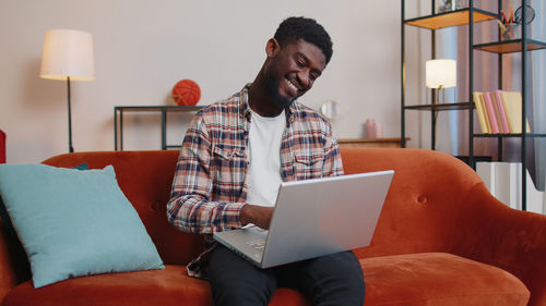 Smiling man using laptop sitting on sofa at home