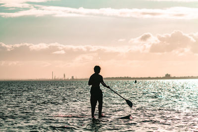 Silhouette man standing in sea against sky during sunset