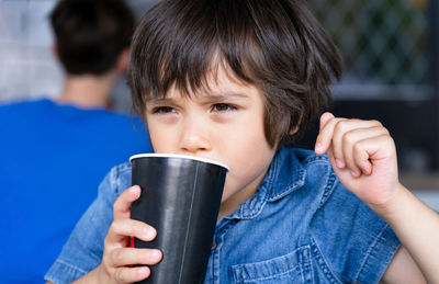 Cute toddler boy drinking cold drink, child sitting in cafe drinking soda or soft drink 