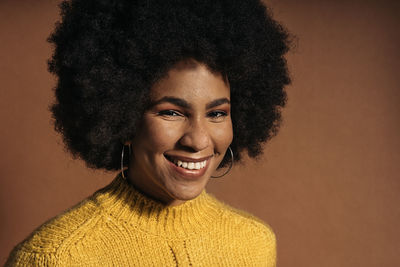 Portrait of young woman standing against brown background