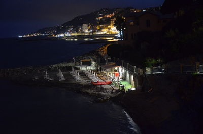 Illuminated buildings by sea against sky at night