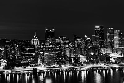 Illuminated buildings by river against sky in city at night