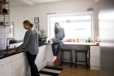 Mother working while daughter using laptop in kitchen at new home