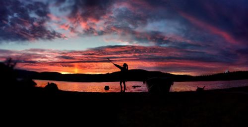 Silhouette woman standing against river and cloudy sky during sunset