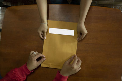 Directly above shot of cropped hands holding envelope at table