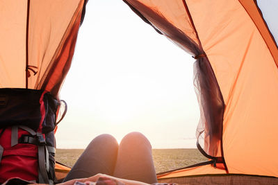 Low section of man relaxing at tent against sky
